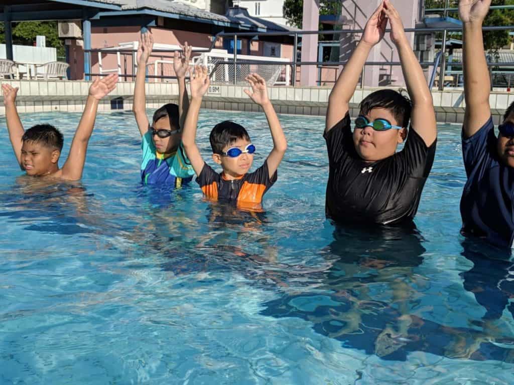 Children participating in swimming lessons in Singapore with a certified instructor teaching water safety skills.