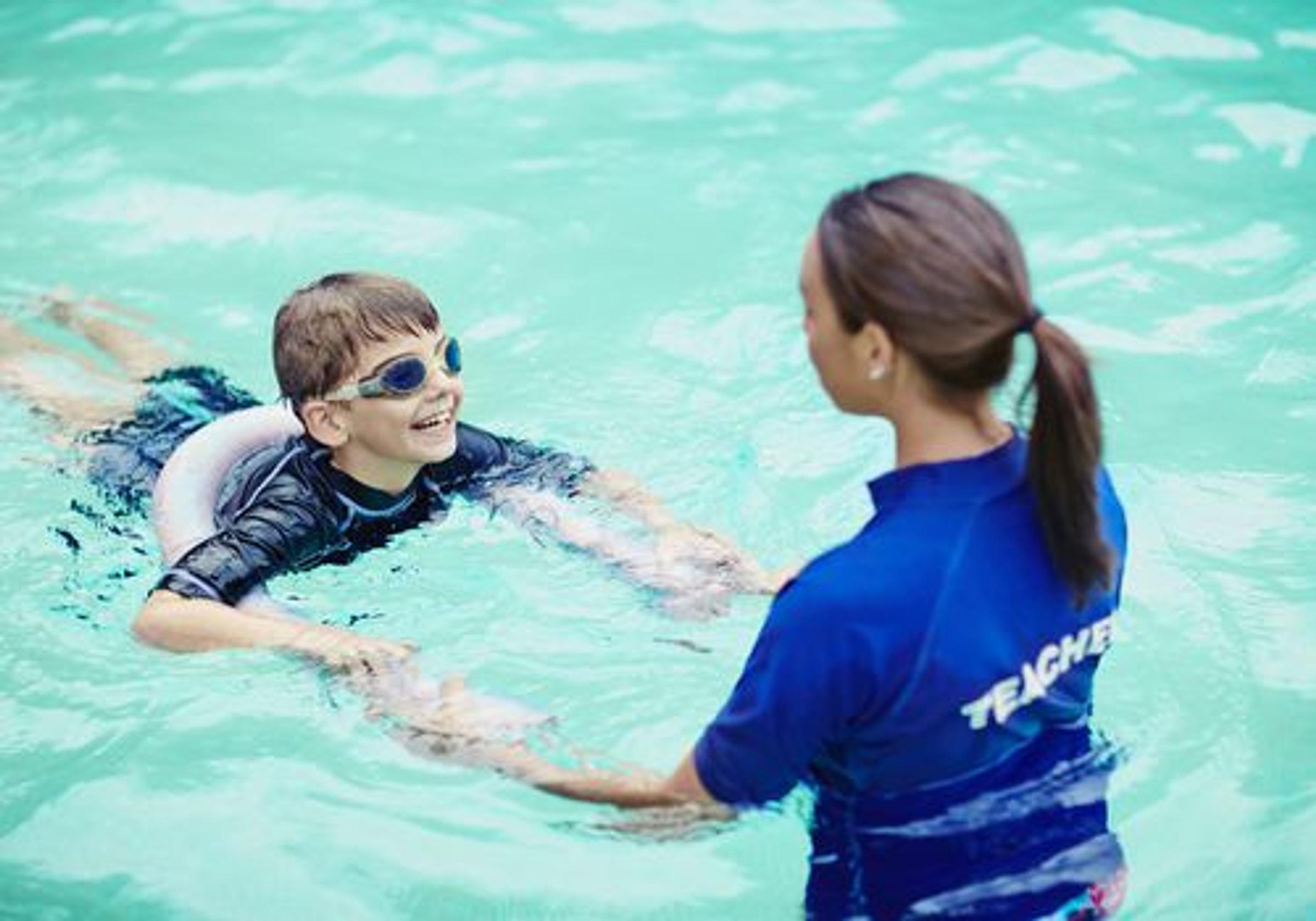 Swimming instructor teaching a child basic swimming techniques during a beginner swimming lesson in Singapore.