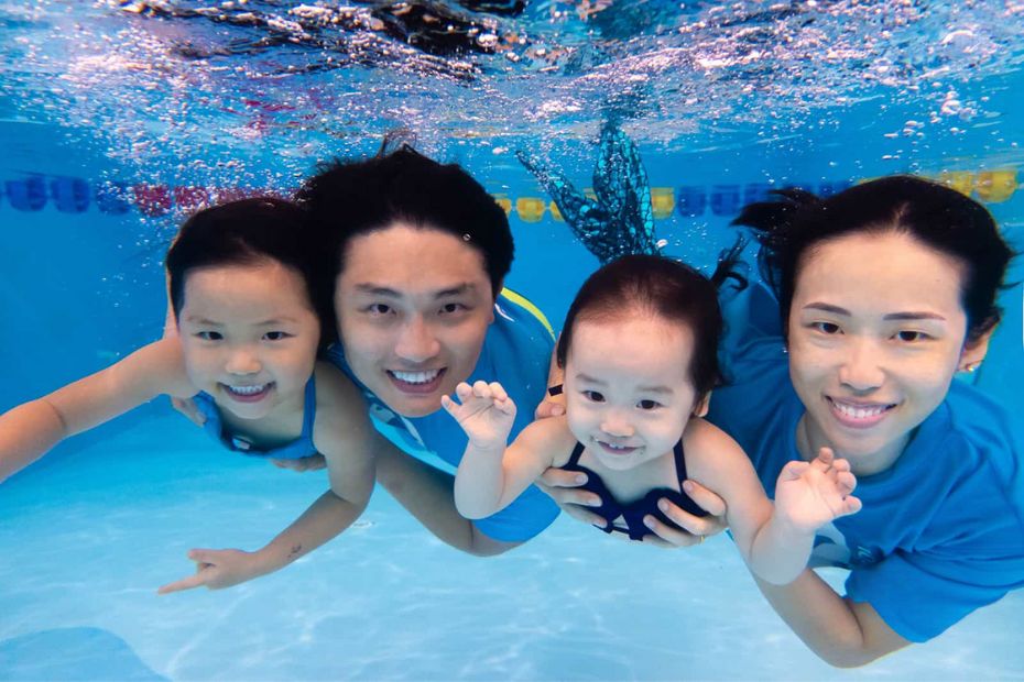 Family enjoying swimming lessons together in Singapore with children practicing underwater swimming skills.
