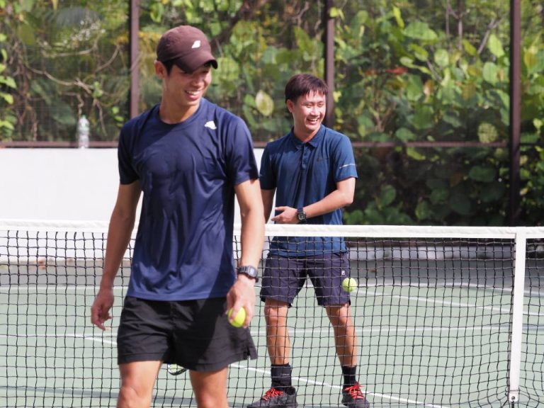Tennis coach guiding students during a private tennis lesson on a Singapore outdoor tennis court.