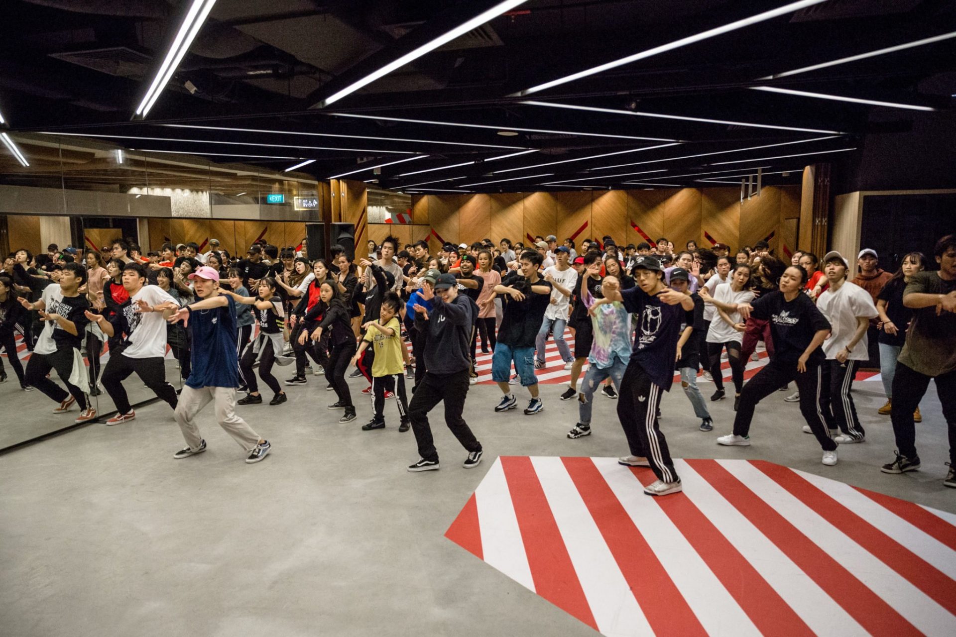 Large hip-hop dance class in Singapore with dancers practicing choreography in a professional studio.